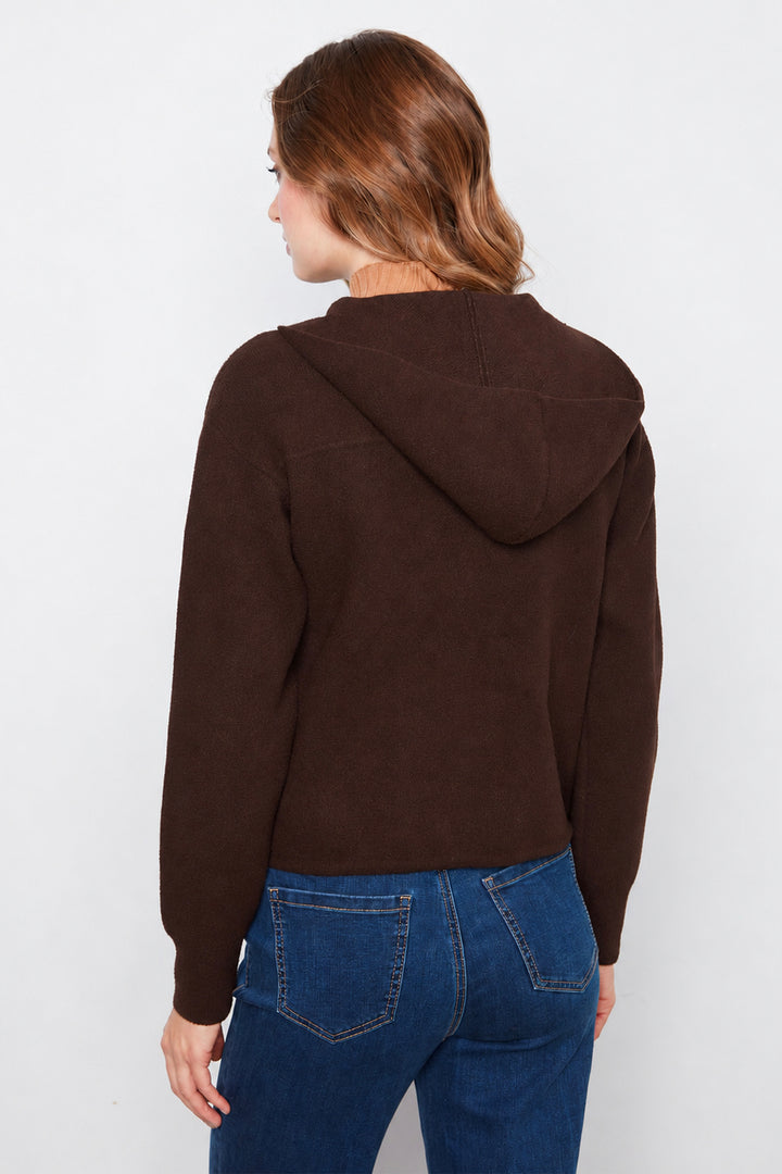 A woman shown from the back wearing a dark brown hooded sweater and blue jeans against a plain light gray studio background.