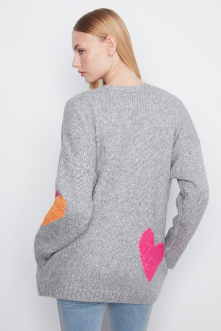 A woman shown from the back wearing a heather gray knit sweater with a large pink heart on the lower back and an orange heart on the sleeve, paired with light blue jeans against a plain white background.