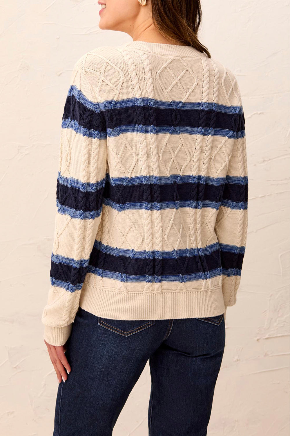 Person wearing a cream sweater with blue and navy striped pattern and dark jeans against a light background
