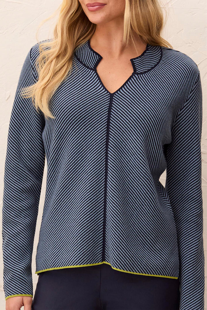 A woman wearing a navy blue and white striped long-sleeve knit top with a split V-neckline and a thin yellow-green piping trim along the collar, hem, and cuffs.