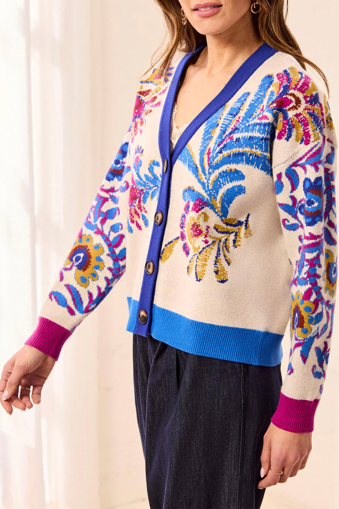 A woman wearing a cream knit cardigan with vibrant blue, pink, and yellow floral embroidery, paired with dark navy pants.