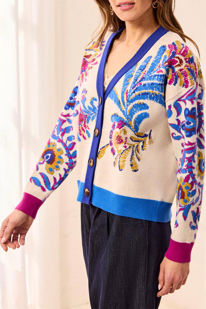 A woman wearing a cream knit cardigan with vibrant blue, pink, and yellow floral embroidery, paired with dark navy pants.