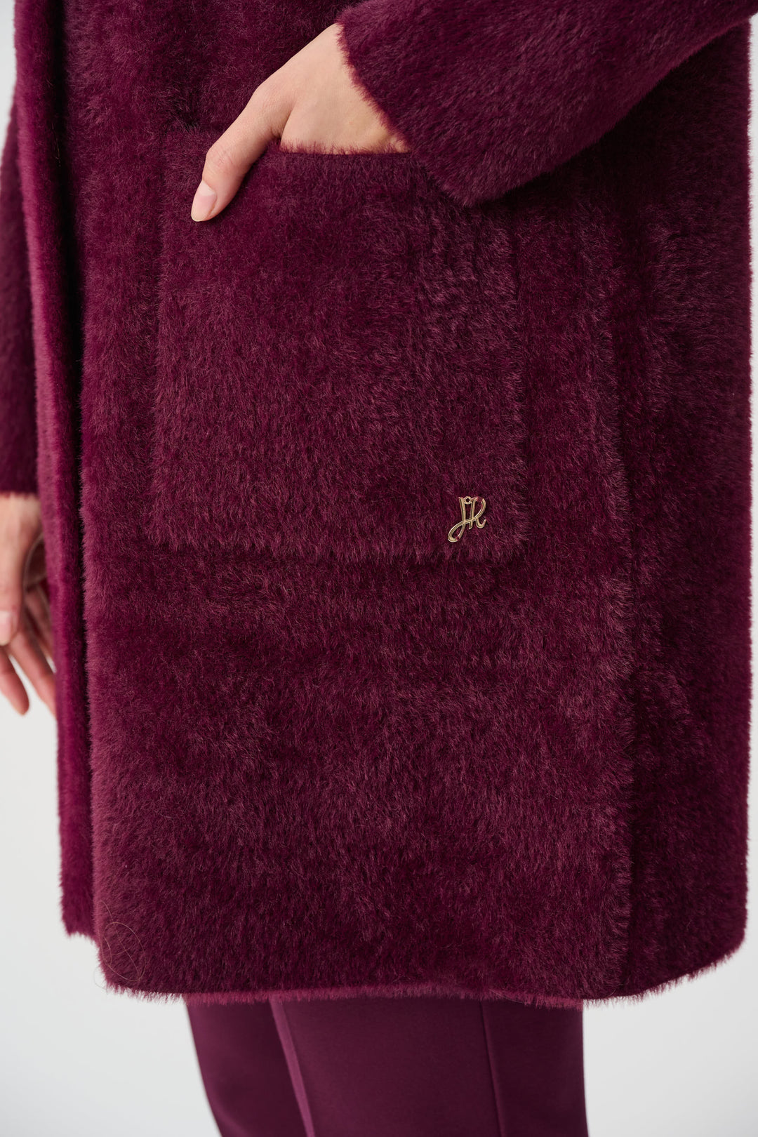 Close-up of a maroon textured coat with a brand logo on a white background