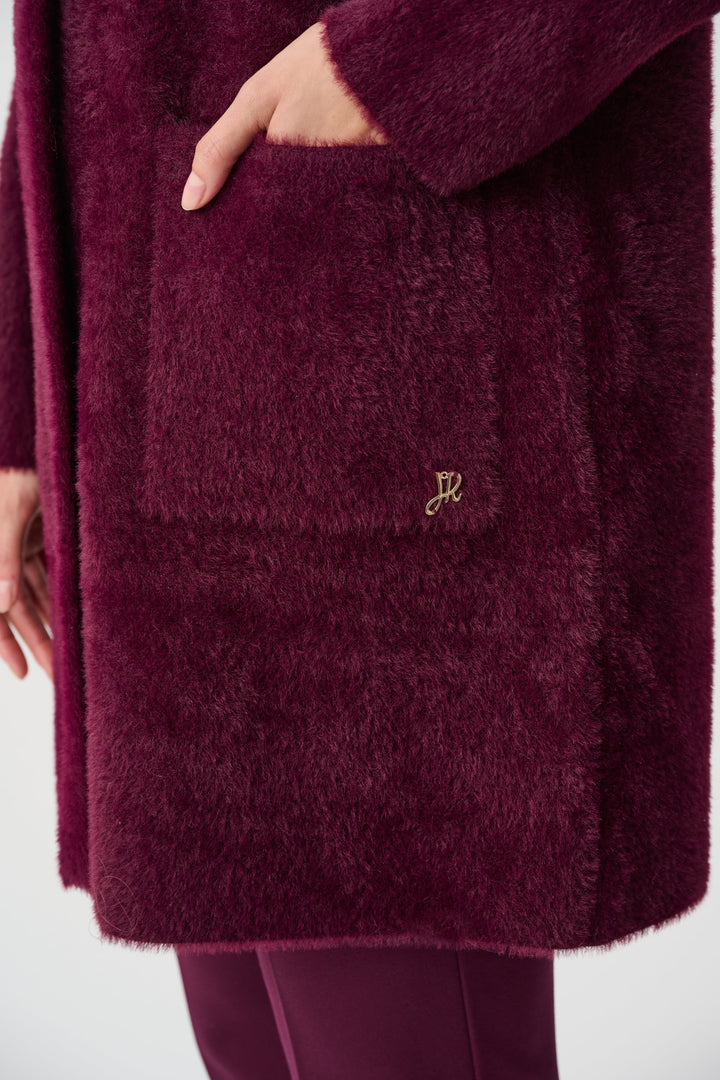 Close-up of a maroon textured coat with a brand logo on a white background