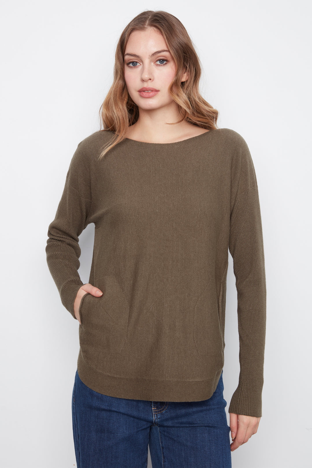 A woman modeling a long-sleeve knit sweater in a muted olive-brown color, paired with blue jeans, against a plain light gray studio background.