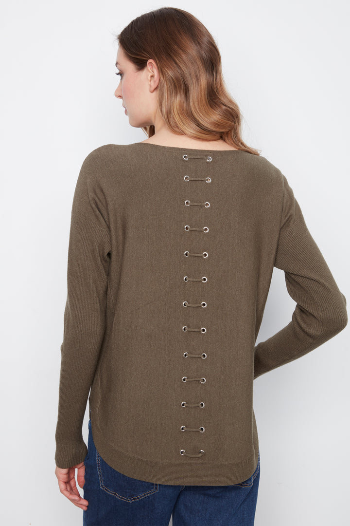 A woman shown from the back wearing a long-sleeve knit top in a muted taupe-brown color, featuring a vertical row of metal eyelets down the center back. She is also wearing blue jeans, set against a plain light gray studio background.