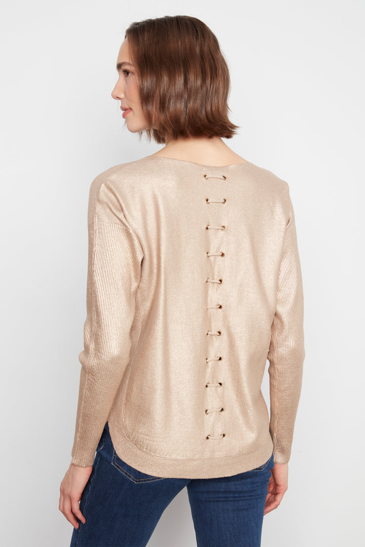 A woman shown from the back wearing a metallic champagne-gold long-sleeve top with a vertical row of lace-up details down the center, paired with blue jeans, against a plain light gray background.