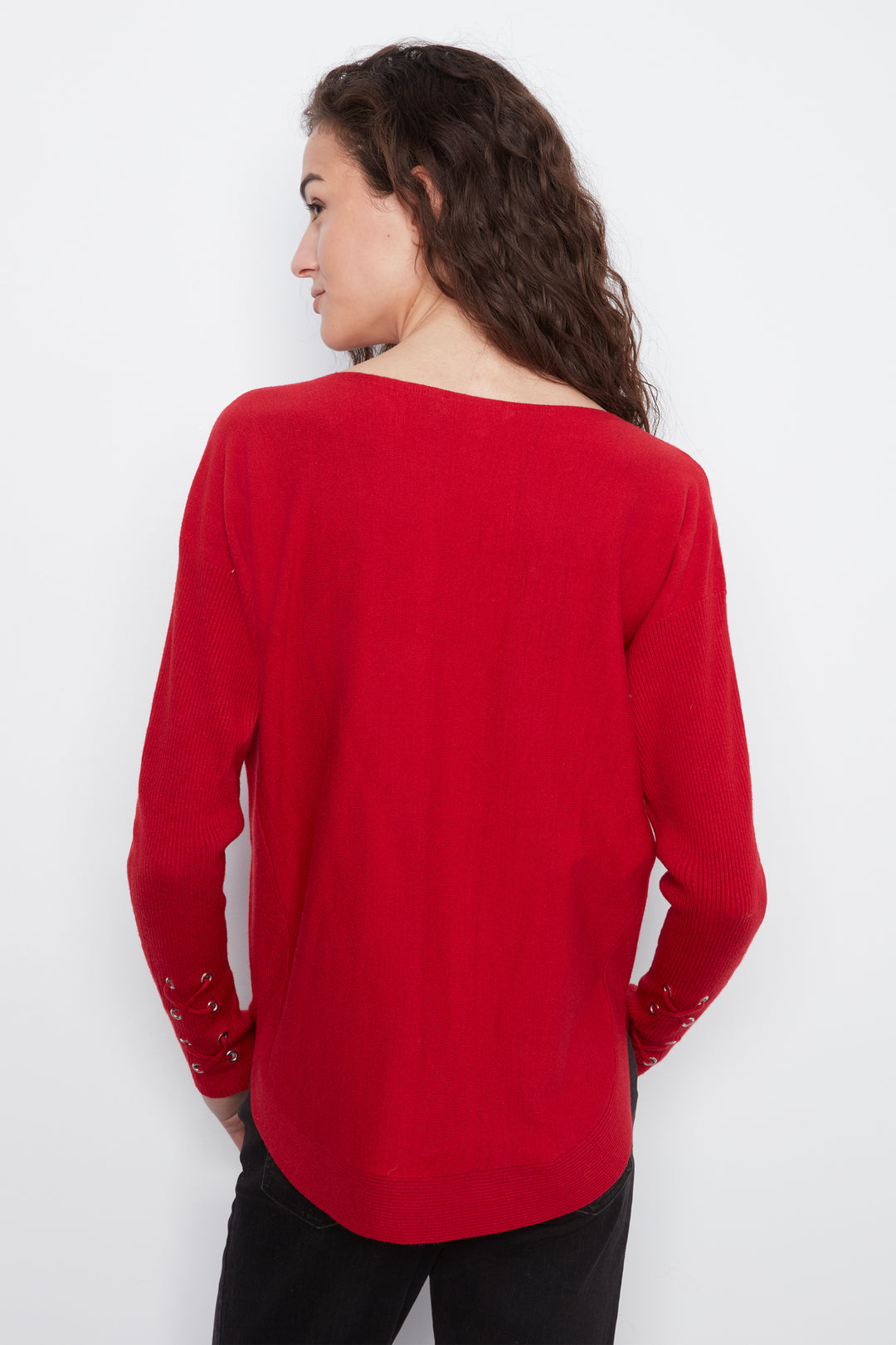 A woman shown from the back wearing a bright red long-sleeve top with lace-up cuff details, paired with black pants, against a plain white background.