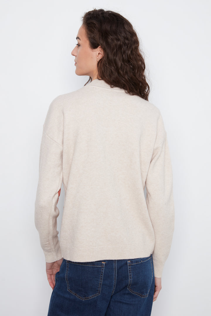 A woman with long, wavy brown hair is shown from the back wearing a light beige knit sweater and dark blue jeans against a plain white background.