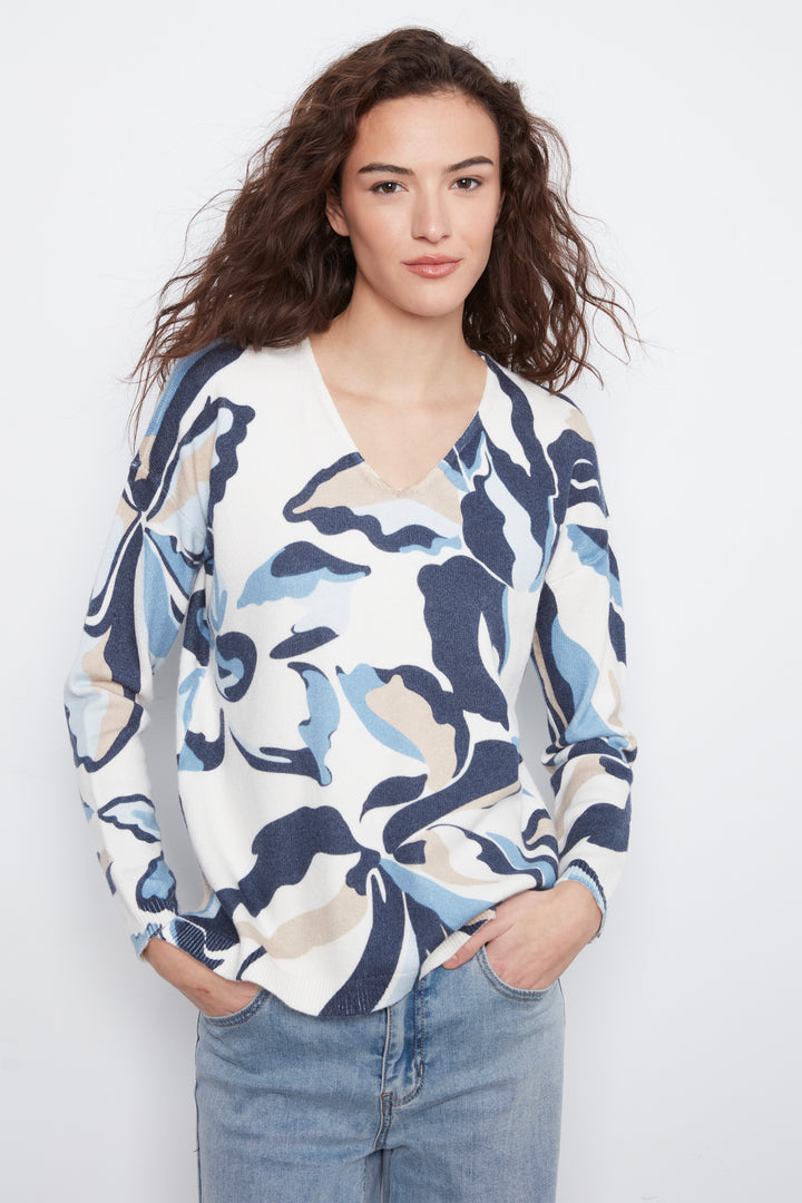 A woman modeling a long-sleeve V-neck wrap top with an abstract floral pattern in navy blue, light blue, and beige on a white background, paired with light-wash blue jeans.