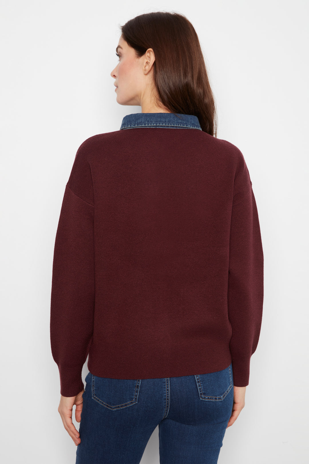 A woman shown from the back wearing a dark burgundy knit sweater with a blue denim collar, paired with blue jeans, against a plain white background.