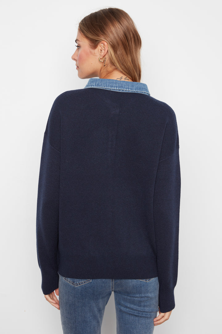 A woman shown from the back wearing a navy blue knit sweater with a light blue denim collar, paired with blue jeans, against a plain white background.