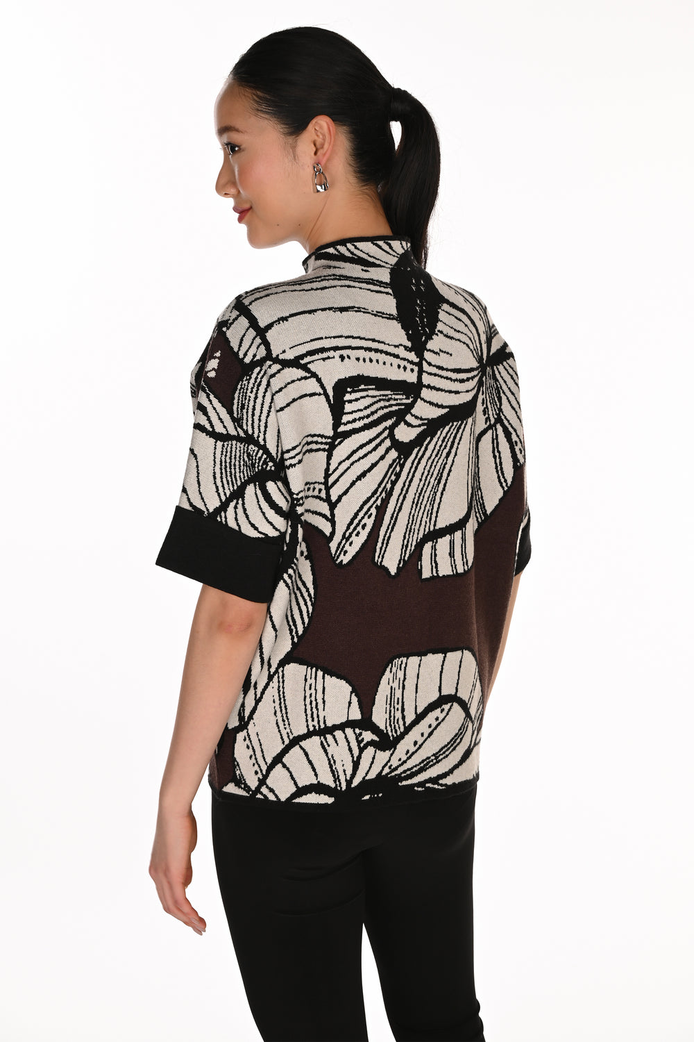 A woman shown from the back wearing a short-sleeve knit top with a black and off-white abstract floral pattern and solid black cuffs, paired with black pants, against a plain white background.