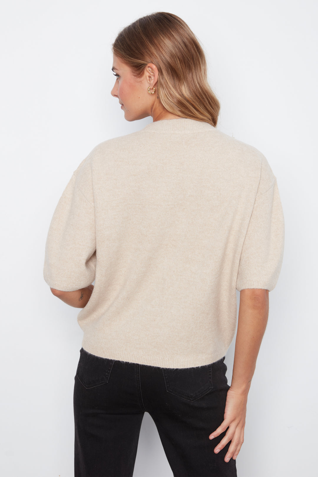 A woman shown from the back wearing a short-sleeve knit sweater in a light cream color, paired with black pants, against a plain white background.