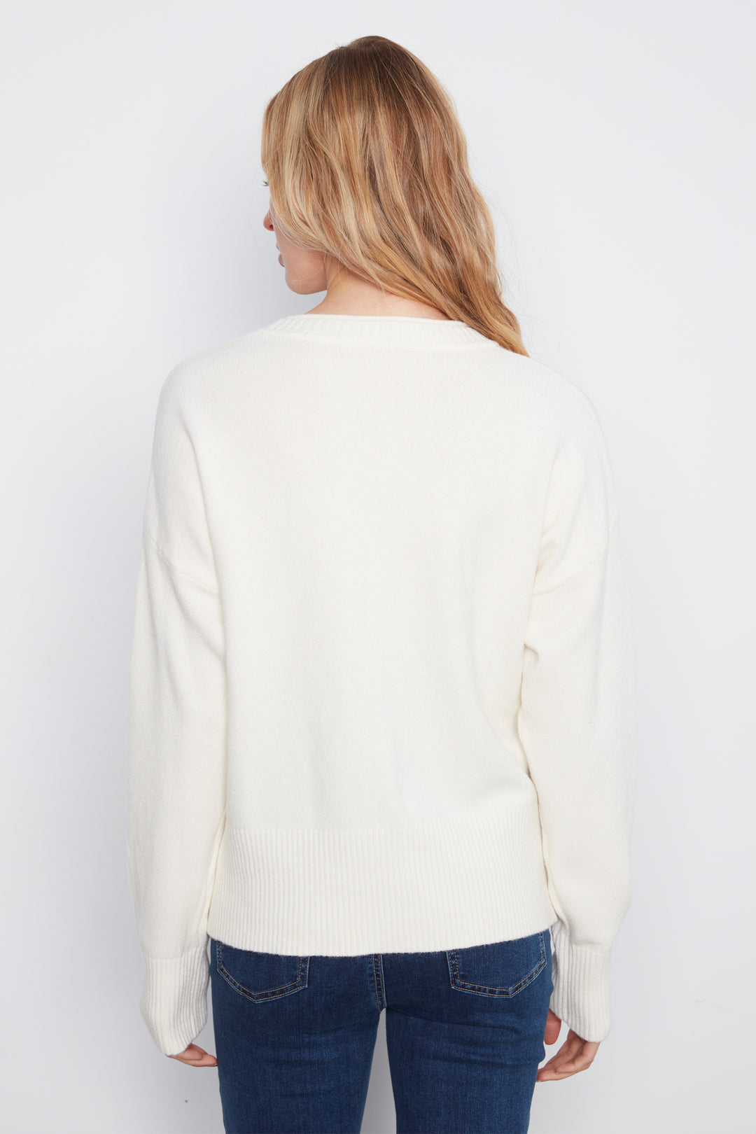 A woman shown from the back wearing a long-sleeve crewneck sweater in cream with a front patch pocket, paired with blue jeans, against a light gray studio background.