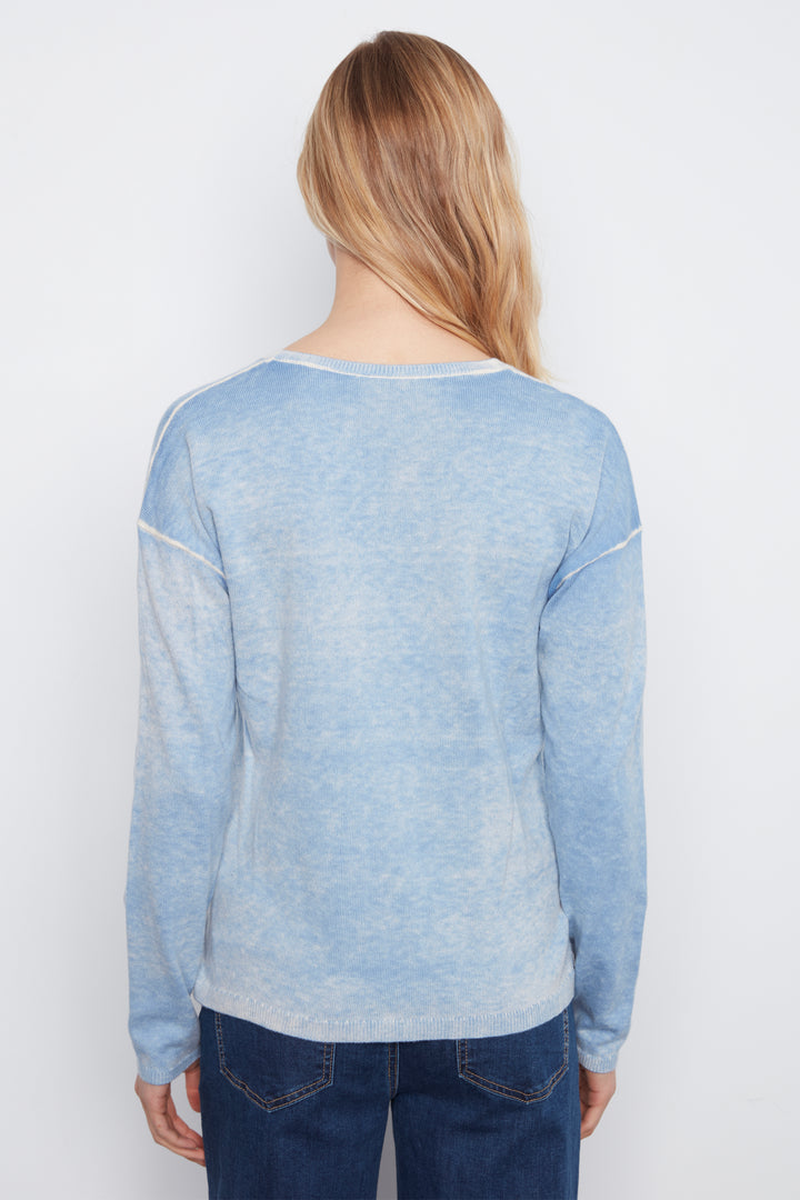 A woman viewed from the back wearing a light blue long-sleeve top with contrast stitching and dark blue jeans, set against a plain white studio background.