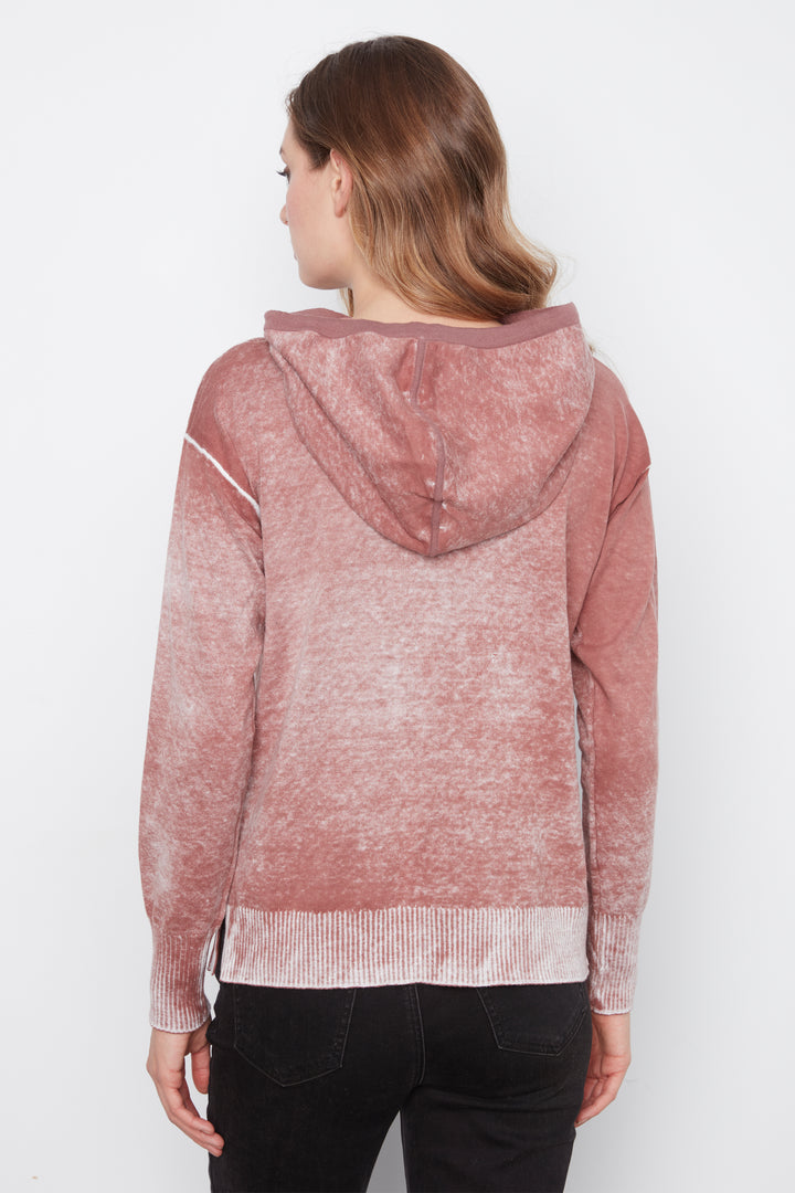 A woman viewed from the back wearing a dusty rose hooded sweater with a marled texture and black pants, set against a plain white studio background.