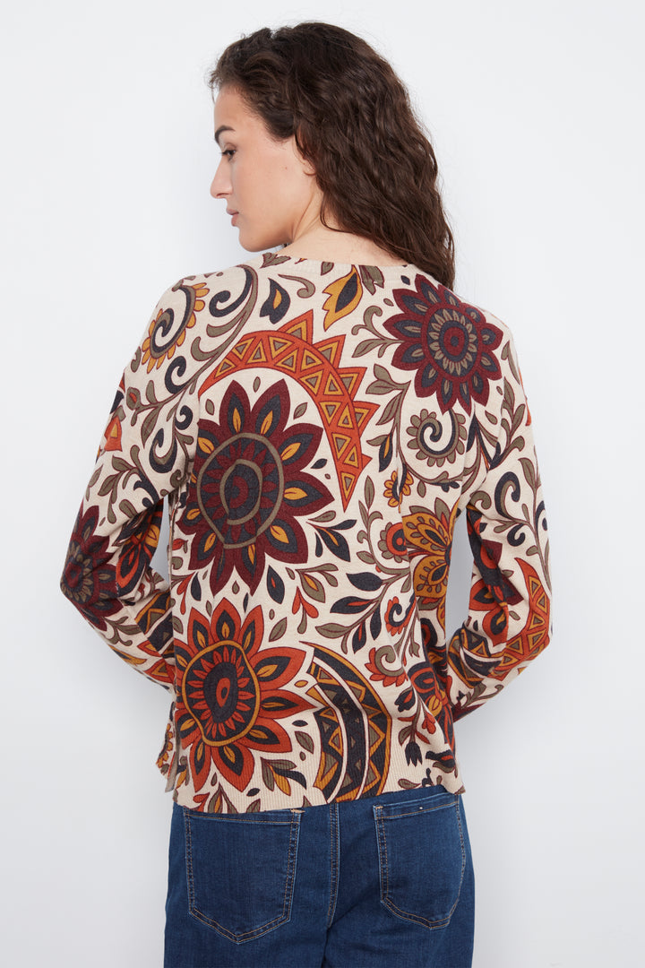 A woman shown from the back wearing a long-sleeve top with a complex, colorful mandala and floral pattern on a cream base, paired with blue jeans against a plain white background.