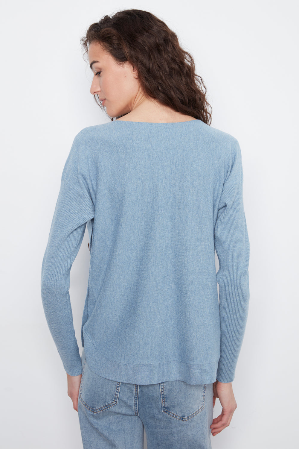 A woman shown from the back wearing a light blue knit sweater and light-wash jeans against a plain white studio background.