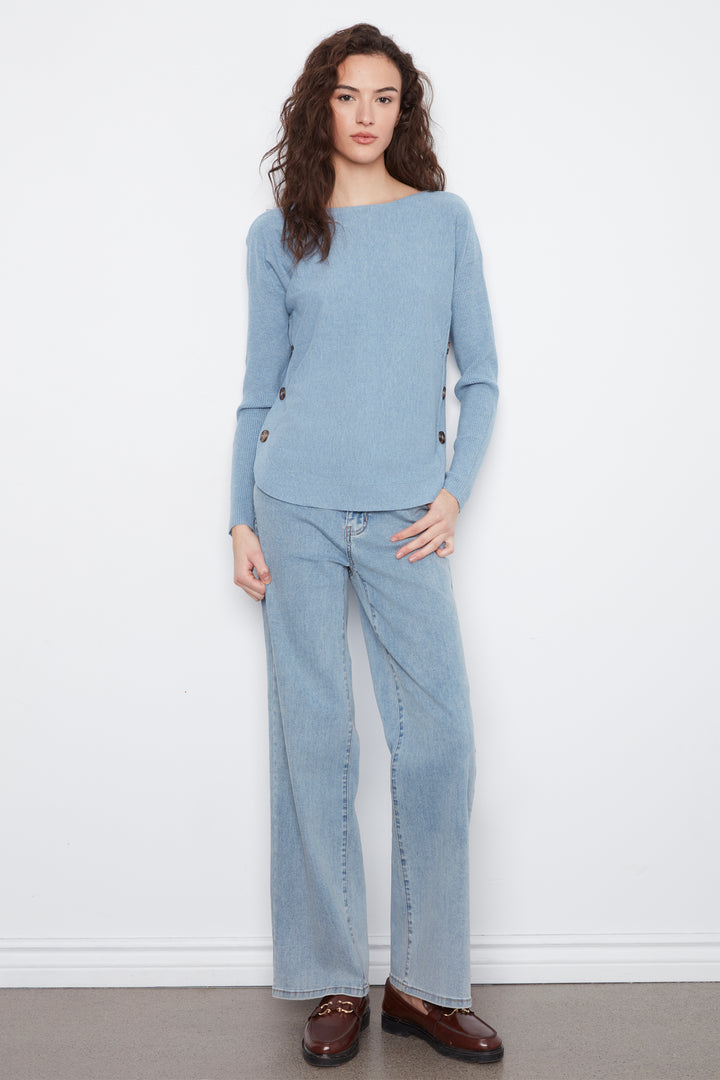 A woman modeling a light blue knit sweater and matching wide-leg jeans against a plain white wall, wearing brown leather loafers.