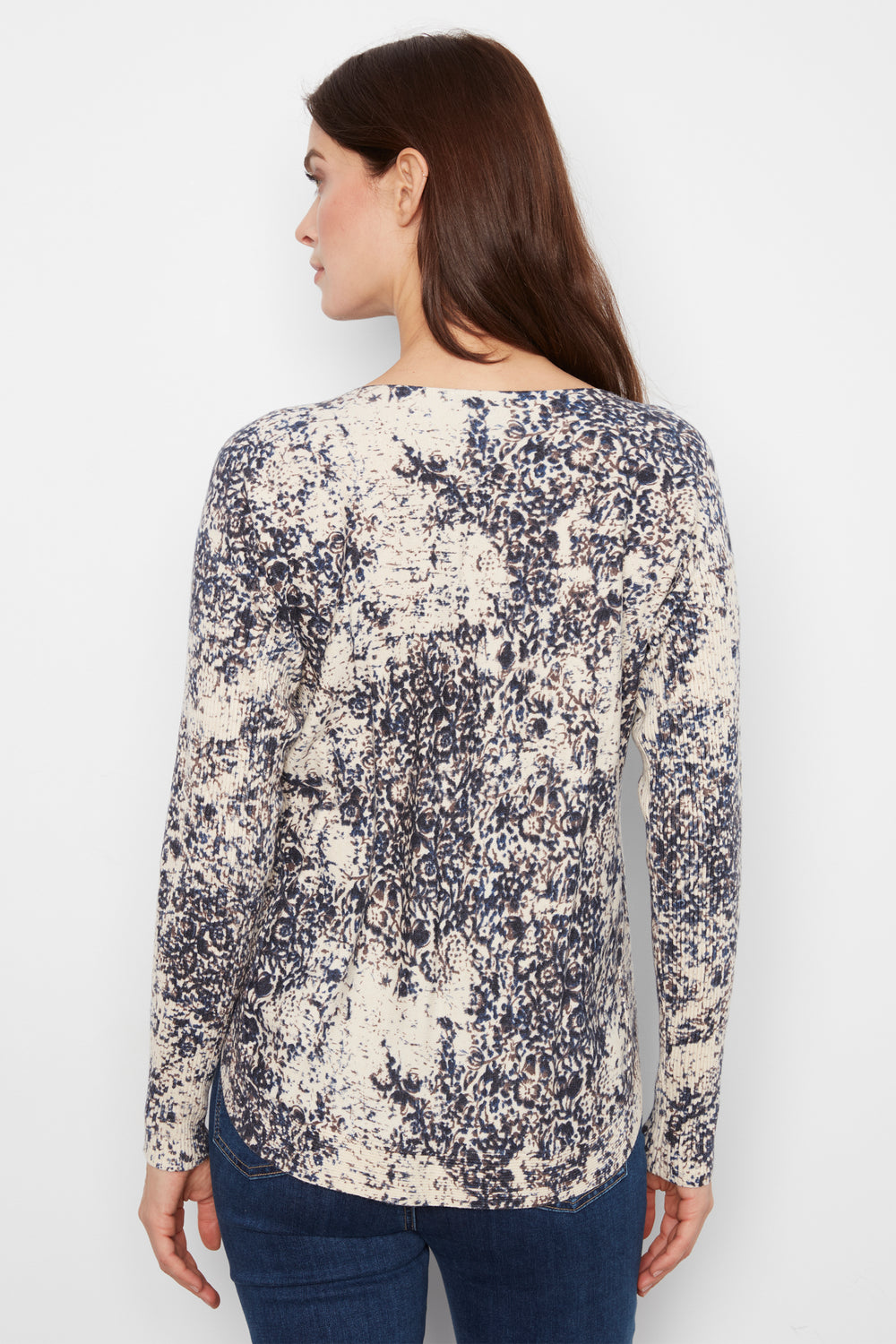 A woman shown from the back wearing a long-sleeve top with an abstract navy and cream pattern, paired with dark blue jeans, against a plain white background.