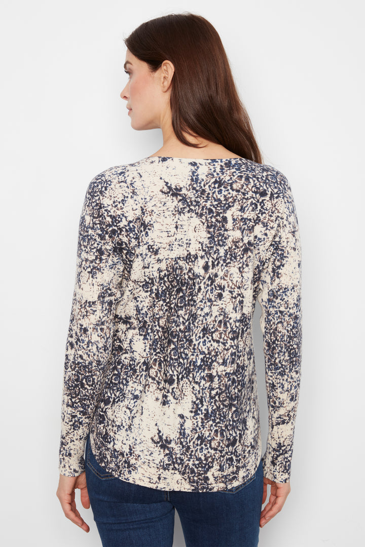 A woman shown from the back wearing a long-sleeve top with an abstract navy and cream pattern, paired with dark blue jeans, against a plain white background.