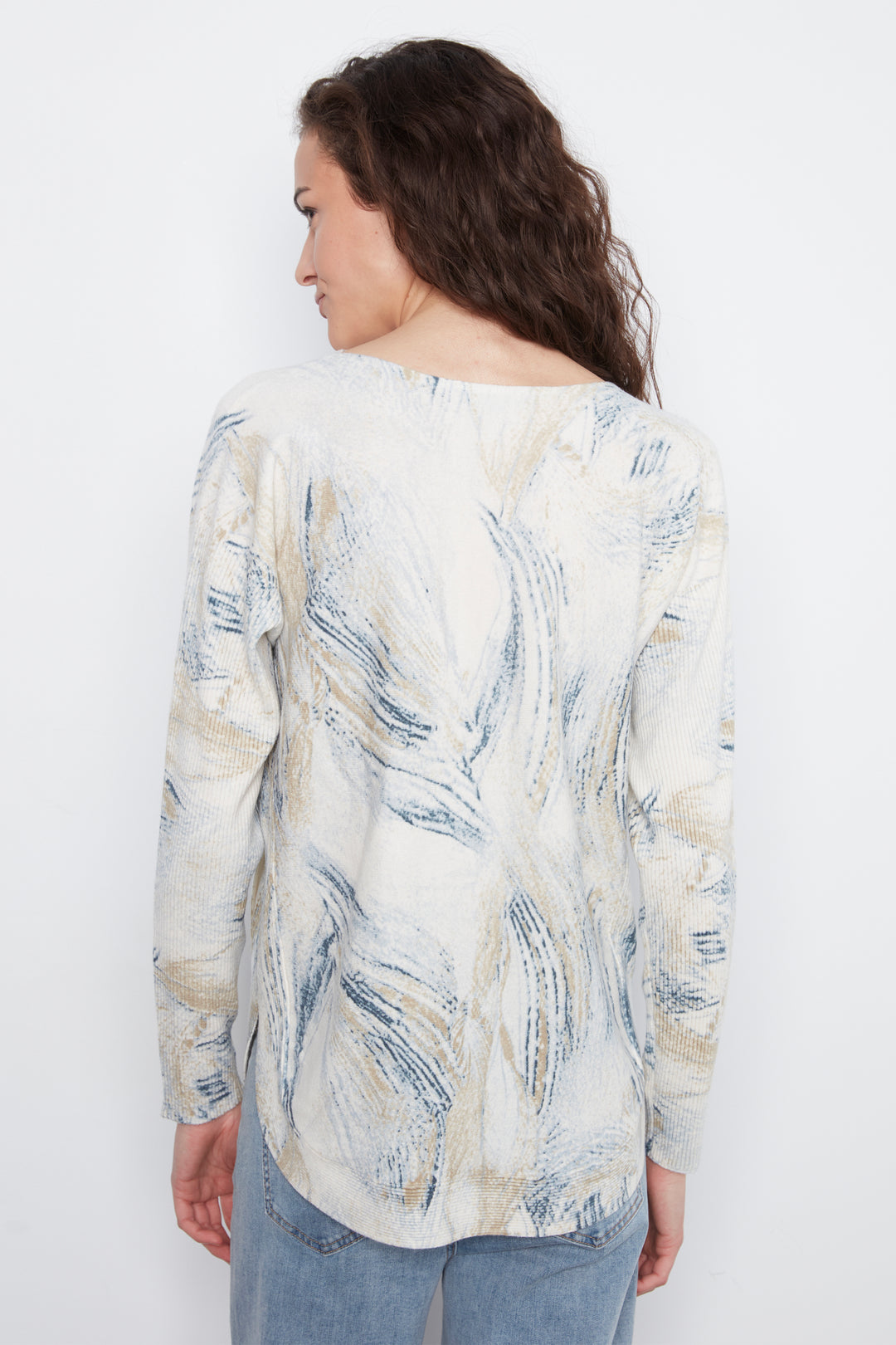A woman shown from the back wearing a long-sleeve blouse with an abstract brushstroke pattern in blue, beige, and white, paired with light blue jeans against a plain white background.