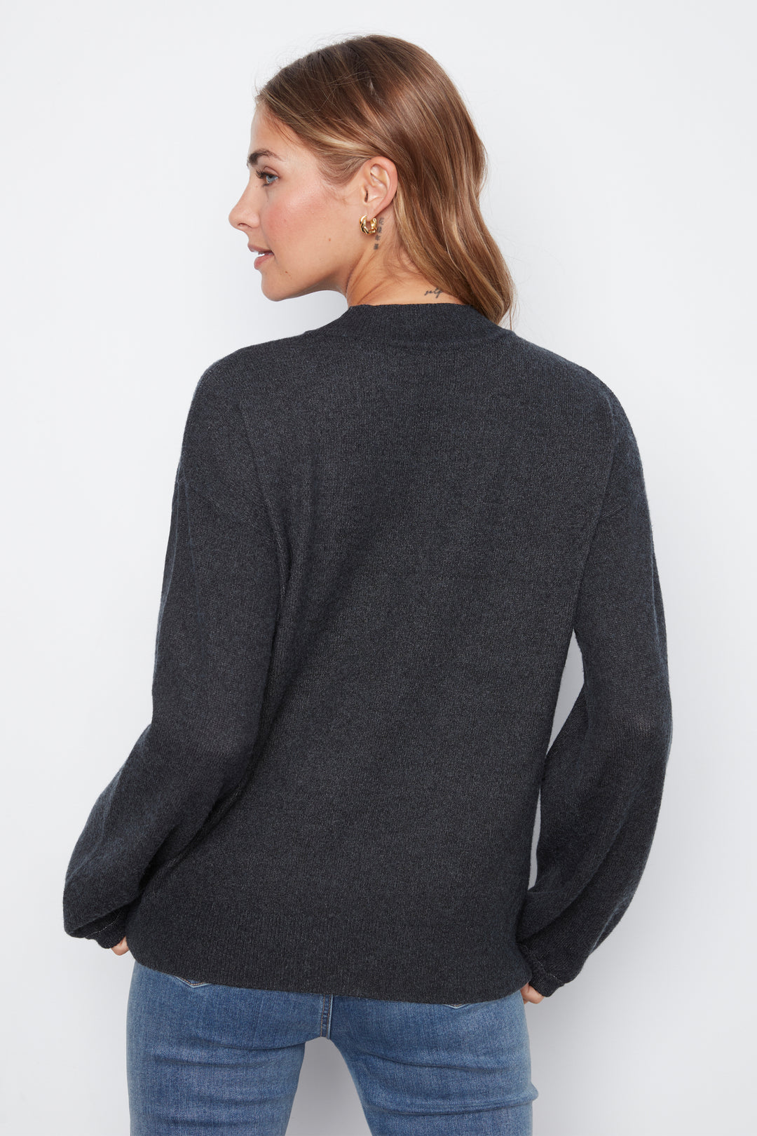 A woman shown from the back wearing a dark charcoal gray knit sweater and blue jeans against a plain white studio background.