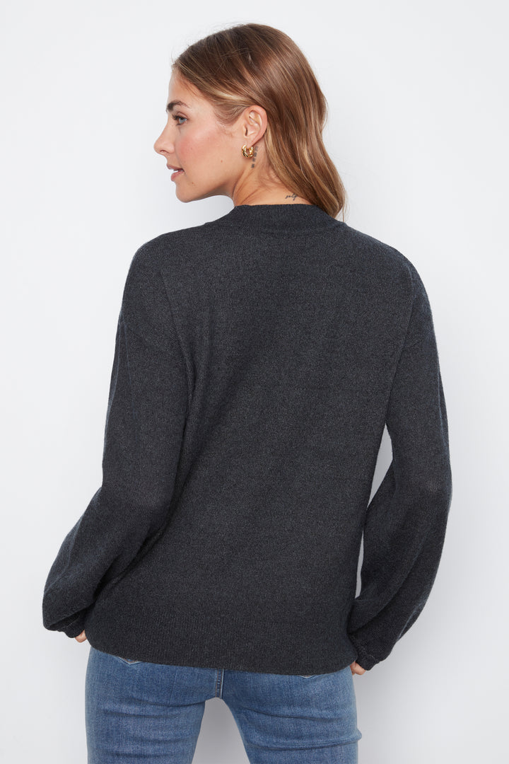 A woman shown from the back wearing a dark charcoal gray knit sweater and blue jeans against a plain white studio background.