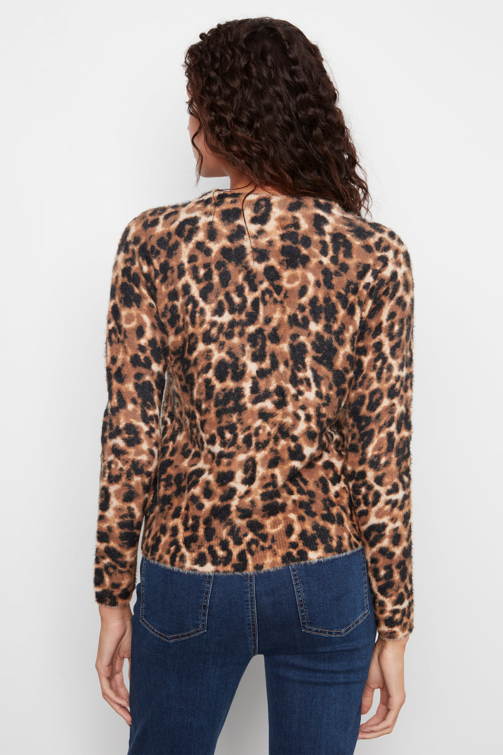 A woman viewed from the back wearing a leopard-print long-sleeve top and blue jeans against a plain light gray studio background.