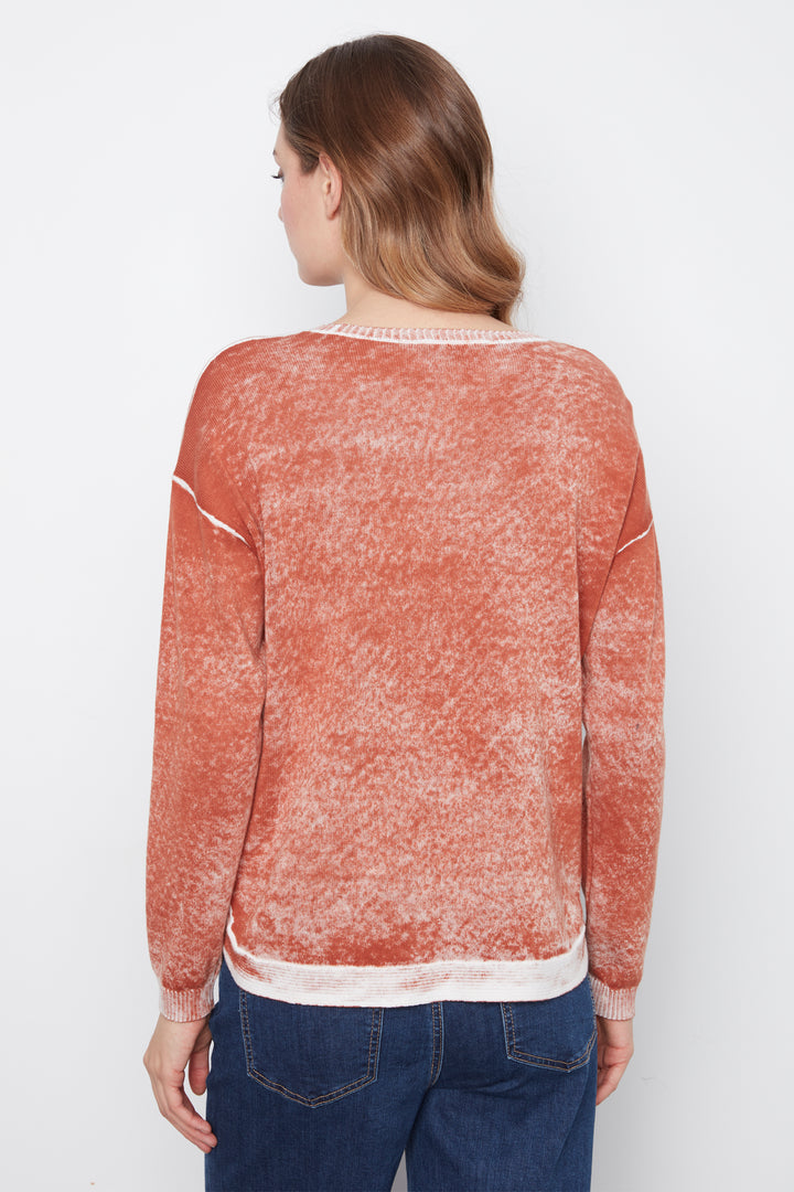 A woman viewed from the back wearing a long-sleeve crewneck sweater with a mottled terracotta orange and white texture, paired with blue jeans, against a plain white background.