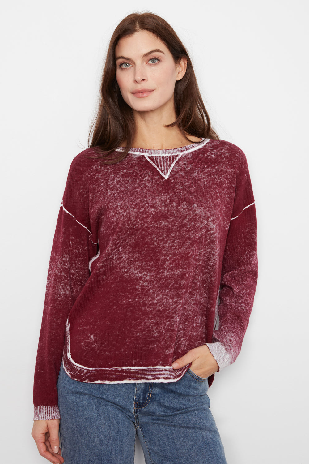 A woman wearing a maroon long-sleeve knit sweater with white contrast stitching and a white V-neck trim, paired with blue jeans, against a plain white background.