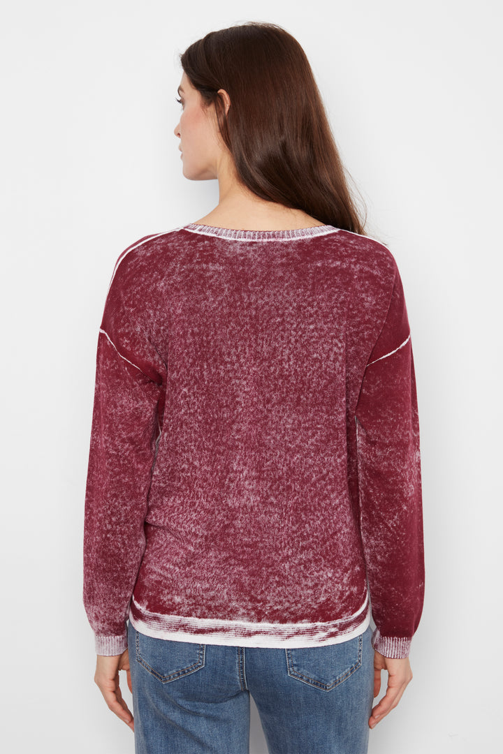 A woman viewed from the back wearing a marled, washed burgundy long-sleeve sweater with white contrast stitching and a white hem, paired with blue jeans against a plain white background.