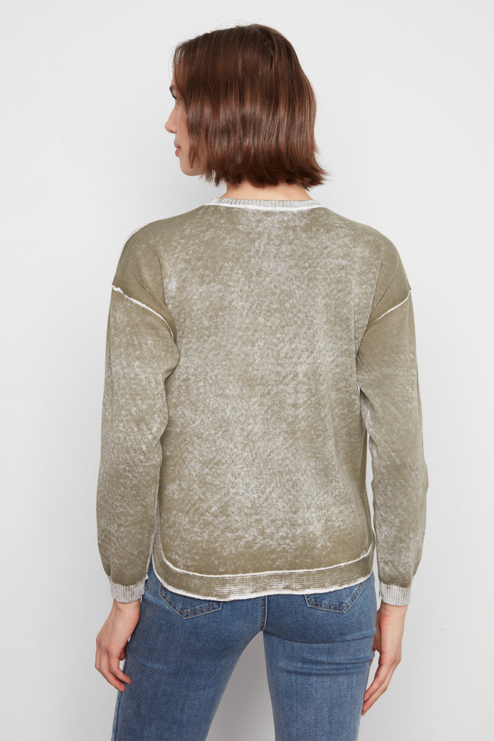 A woman viewed from the back wearing a long-sleeve crewneck sweater with a textured, washed finish in a muted olive-beige color, paired with blue jeans, against a plain light gray background.