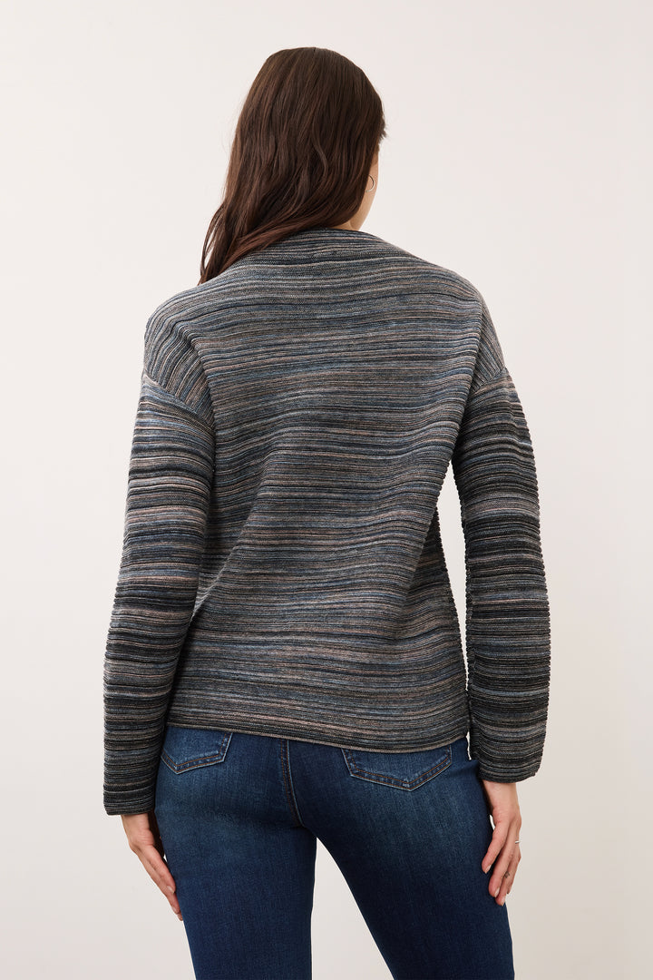 A woman viewed from the back wearing a long-sleeve knit sweater with horizontal gray and navy stripes, paired with dark blue jeans, against a plain off-white studio background.