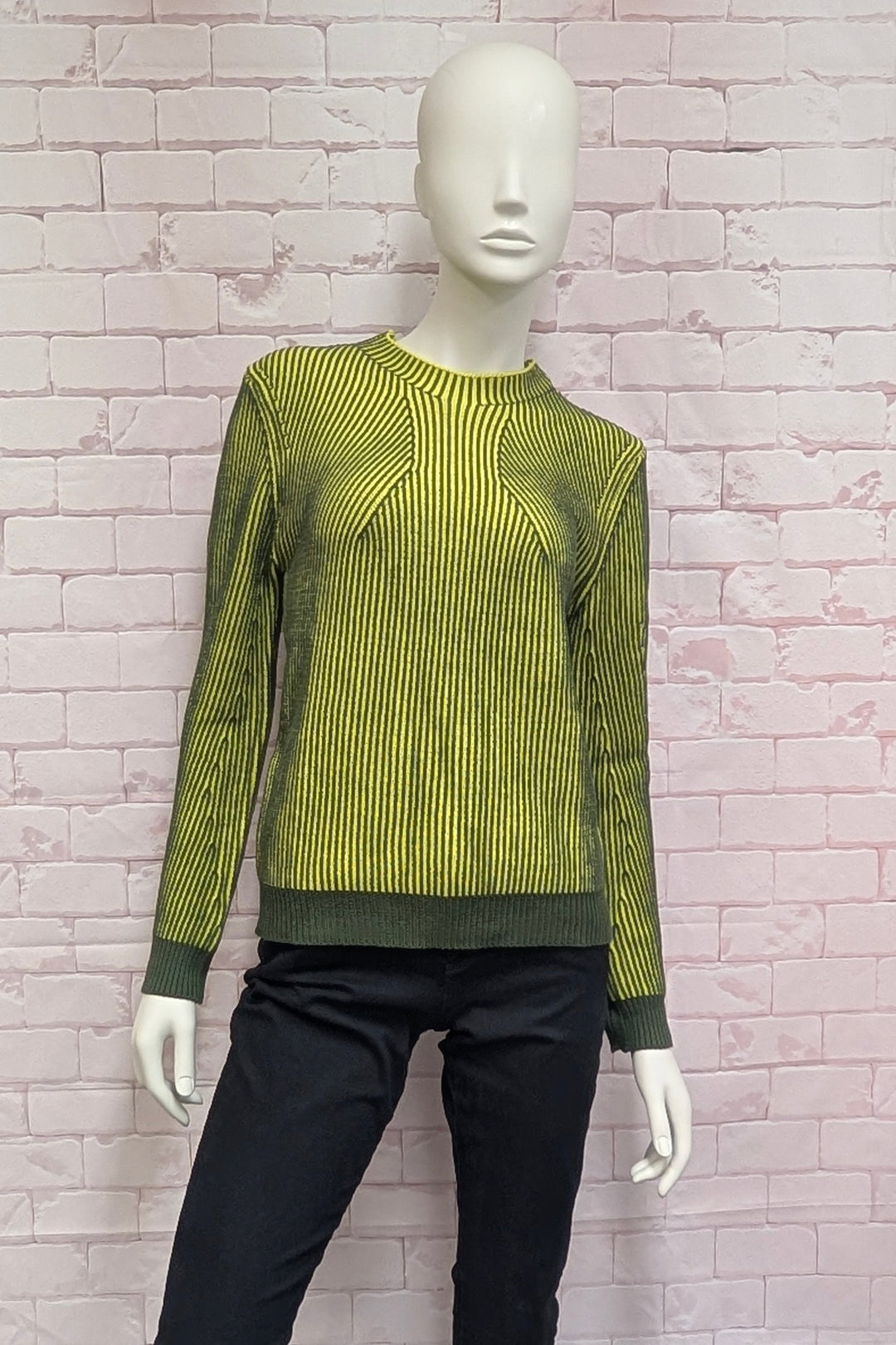A mannequin wearing a long-sleeve knit sweater with vertical lime green and dark olive green stripes, featuring a crew neck and ribbed cuffs and hem.