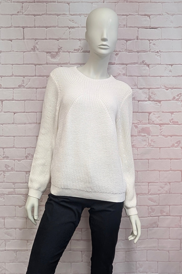A mannequin wearing a off-white ribbed knit crewneck sweater with long sleeves, in front of a white brick background.