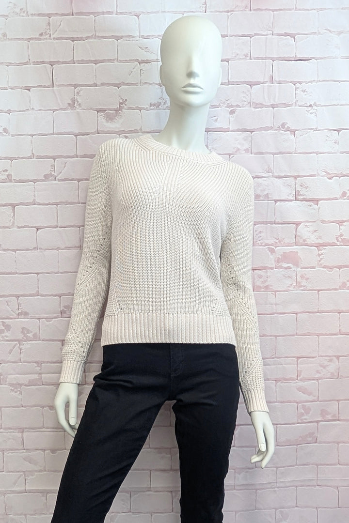 A mannequin wearing a ecru ribbed knit sweater with long sleeves and a crew neck, displayed on pink brick background.