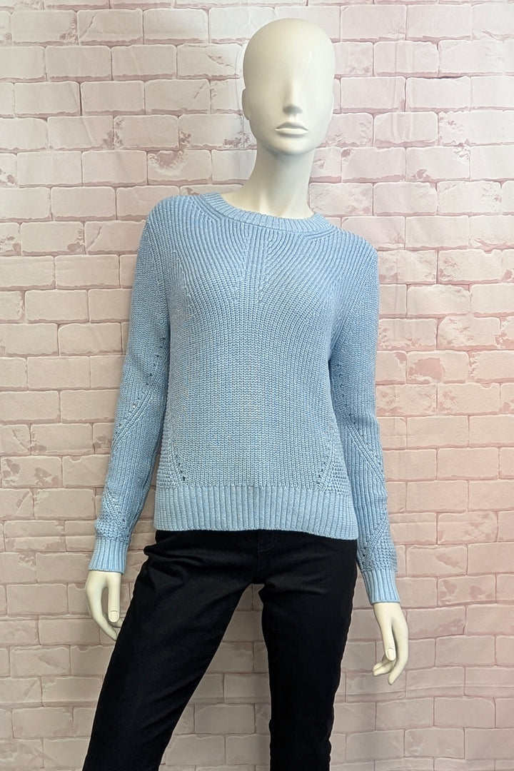 A mannequin wearing a light blue ribbed knit sweater with long sleeves and a crew neck, displayed on pink brick background.