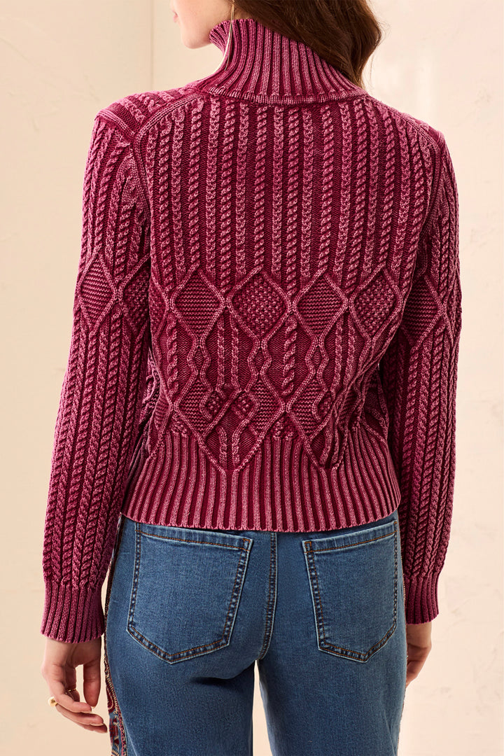A woman shown from the back wearing a textured, cable-knit turtleneck sweater in a deep berry pink, paired with blue jeans.