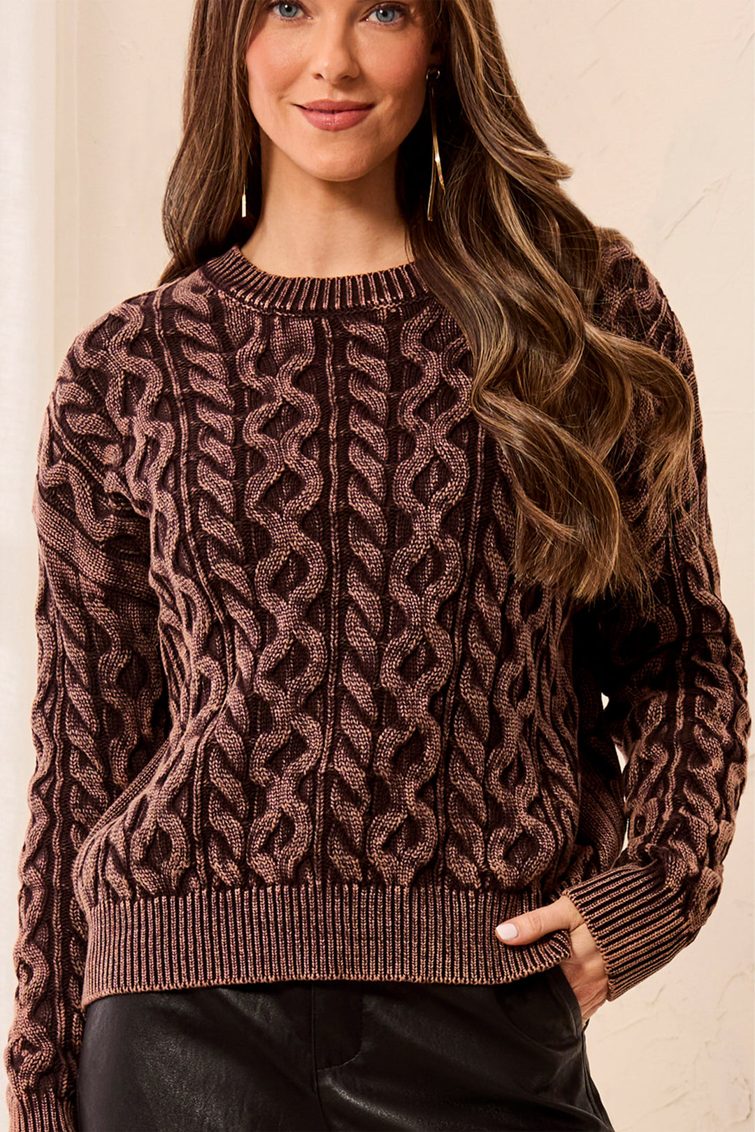 Woman wearing a brown cable knit sweater against a neutral background
