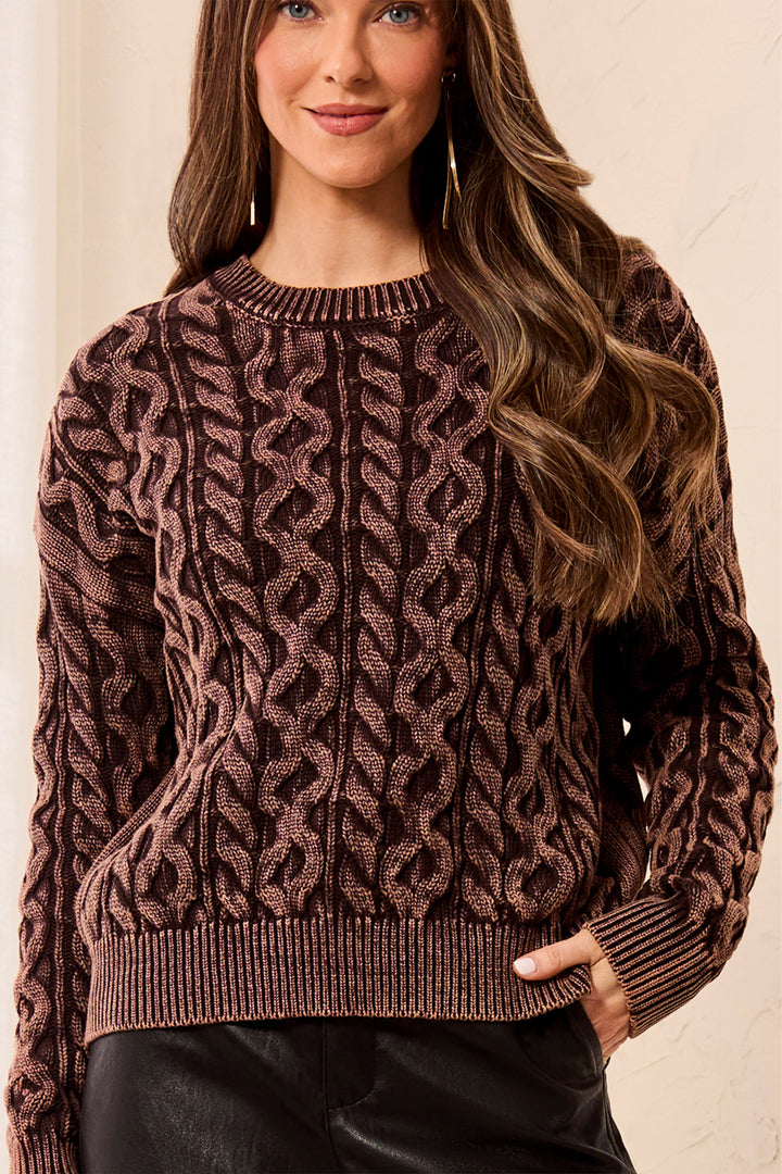 Woman wearing a brown cable knit sweater against a neutral background