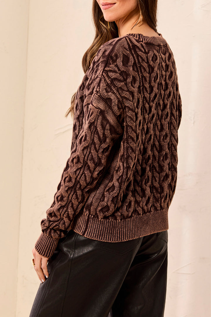 Brown cable knit sweater worn by a person against a neutral background