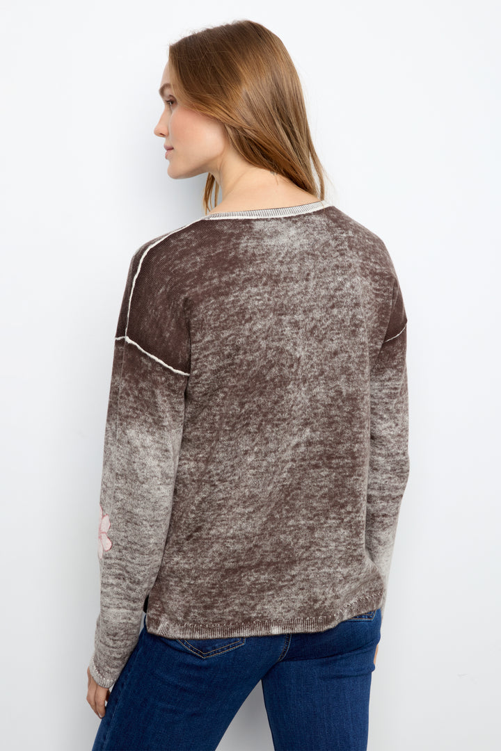 A woman shown from the back wearing a brown and gray marled knit sweater with white contrast stitching, paired with blue jeans, against a plain white background.