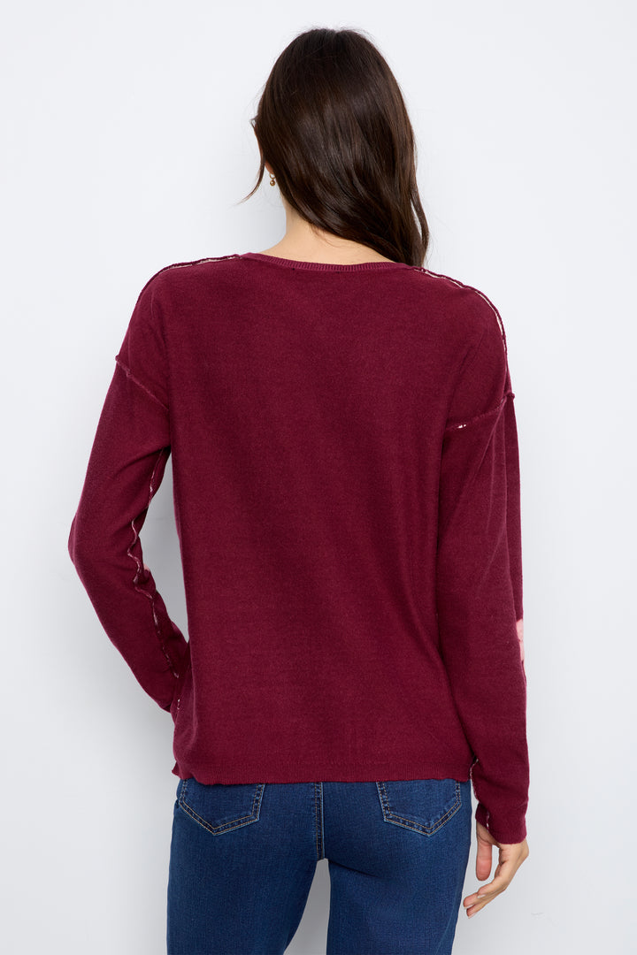 A woman viewed from the back wearing a long-sleeve maroon knit top with distressed details on the sleeves and a small side pocket, paired with blue jeans against a plain white background.