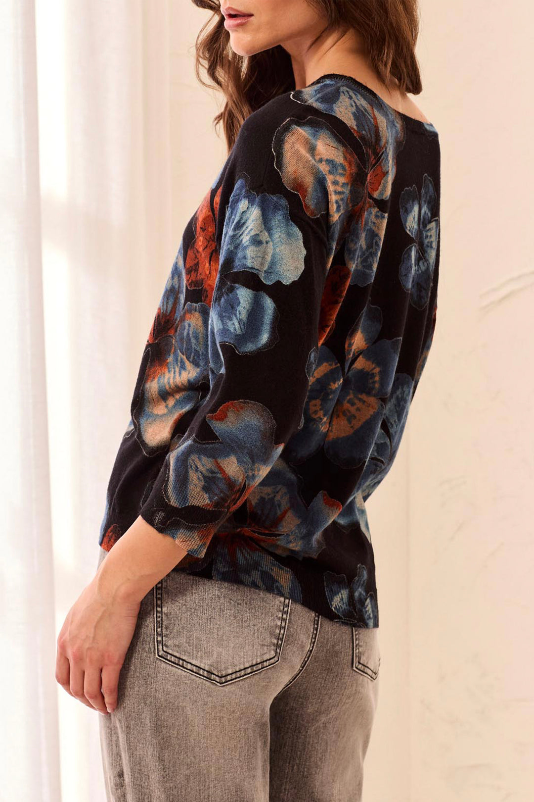 Woman shown from the back wearing a black sweater with blue and orange floral patterns on a neutral background