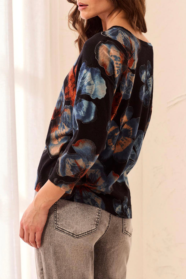 Woman shown from the back wearing a black sweater with blue and orange floral patterns on a neutral background
