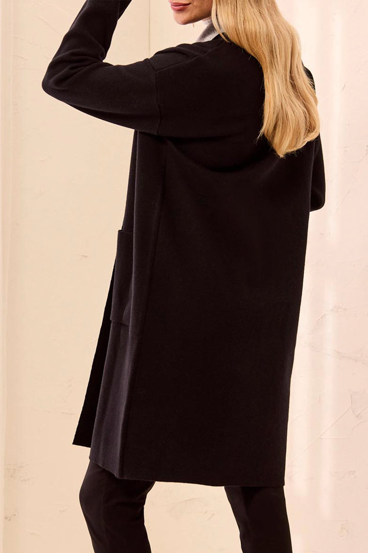 A woman shown from the back wearing a long black open-front cardigan with contrasting light grey trim against a neutral cream background.