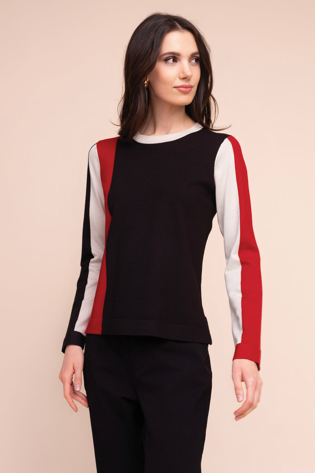 A woman modelling a black sweater with red and white stripes on the sleeves in front of a beige background. 