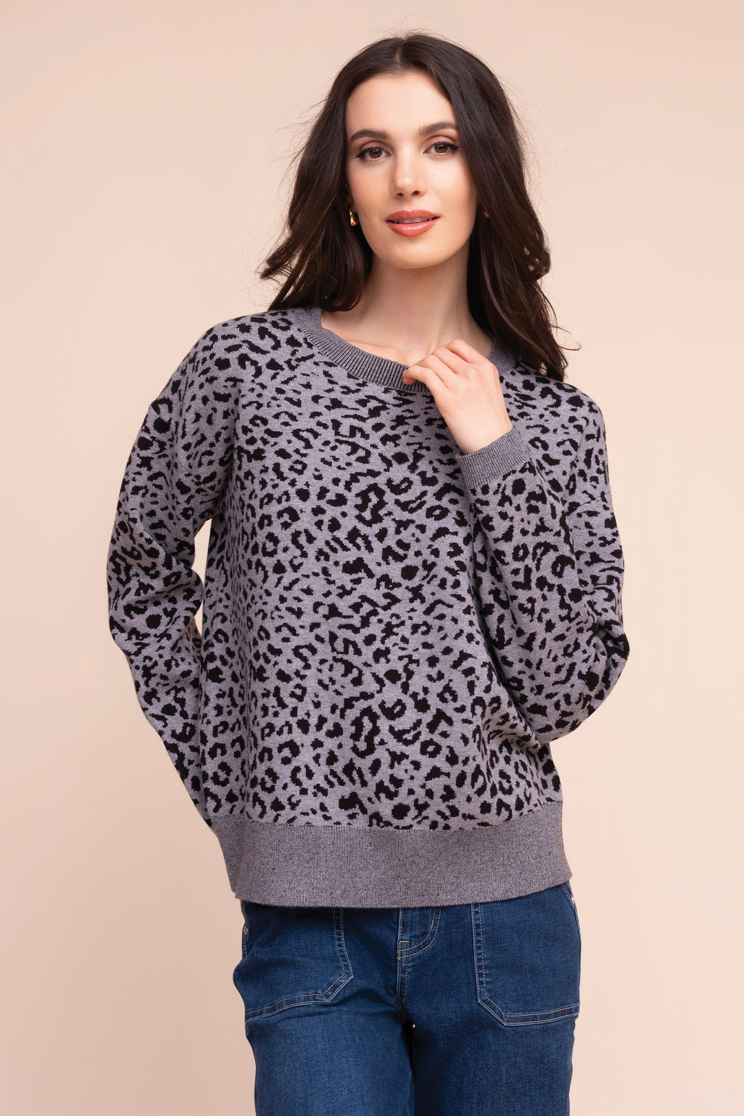 A woman modeling a gray and black leopard print crewneck sweater with ribbed cuffs, collar, and hem, paired with blue jeans against a solid beige background.
